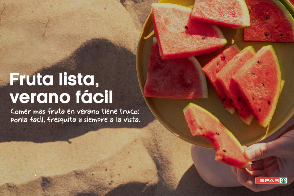 Trozos de sandía servidos en un plato amarillo sobre una superficie de arena, con una mano sosteniendo una porción. La imagen incluye el mensaje “Fruta lista, verano fácil” y el logotipo de SPAR.